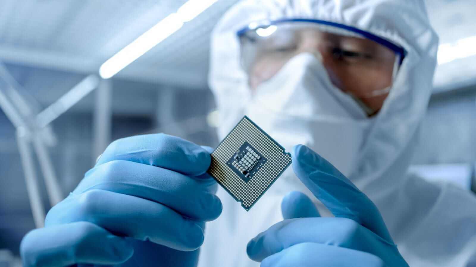 Engineer in Sterile Coverall Holds Microchip with Gloves and Examines it by Gorodenkoff via Shutterstock